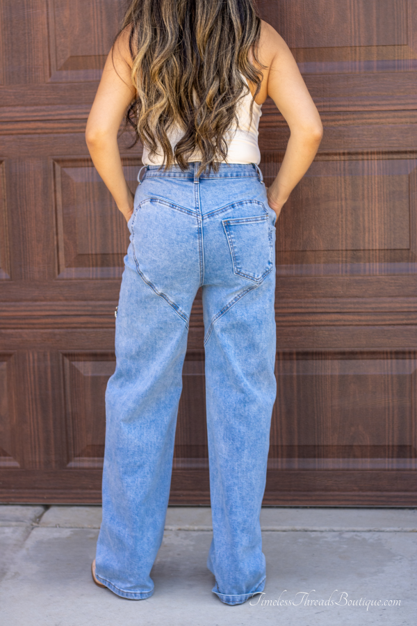 "Shimmer Cut Light Washed Rhinestone Front Denim Jeans with above-the-knee slits adorned with rhinestones and a heart-shaped detail on the back, offering a trendy and glamorous look."