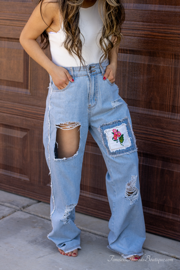 "Rose Garden Stripes Embroidered Denim Pants featuring distressed details, blue stripes, and delicate rose embroidery, made from 100% cotton for a stylish and comfortable fit."