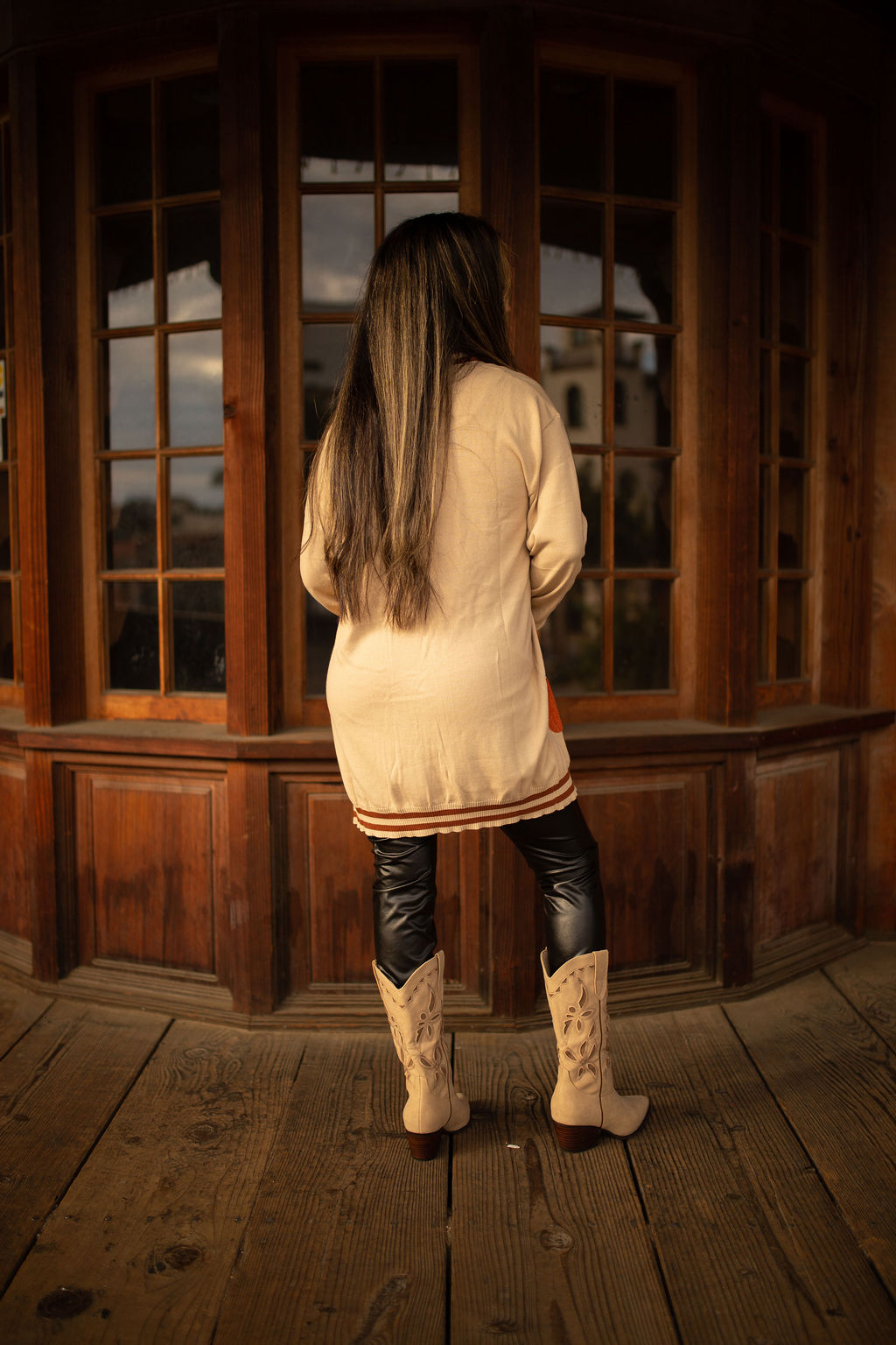 Cream cardigan with striped trim and an embroidered orange pumpkin patch on the lower side, shown in warm outdoor lighting.
