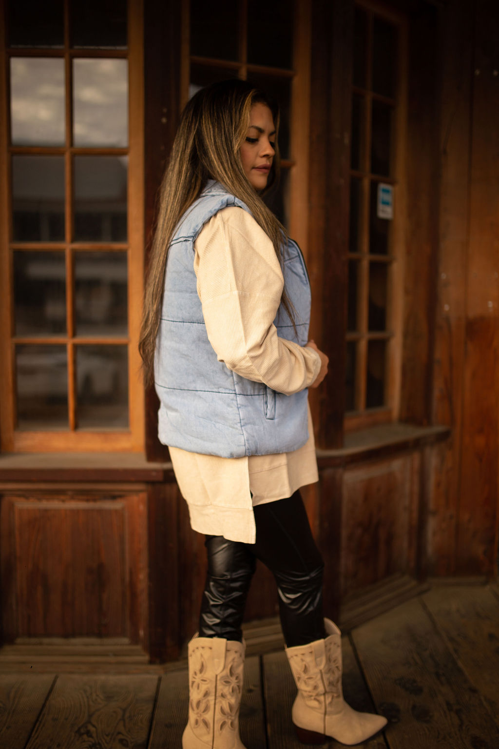 Light-wash denim puffer vest with quilted texture, high collar, and front pockets styled over a neutral long sleeve top.