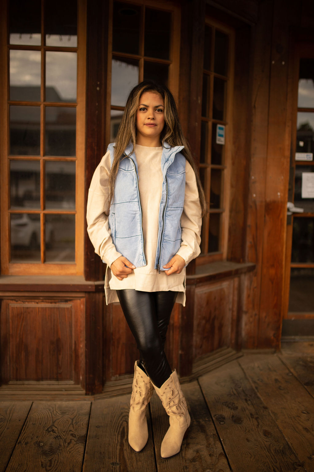 Light-wash denim puffer vest with quilted texture, high collar, and front pockets styled over a neutral long sleeve top.