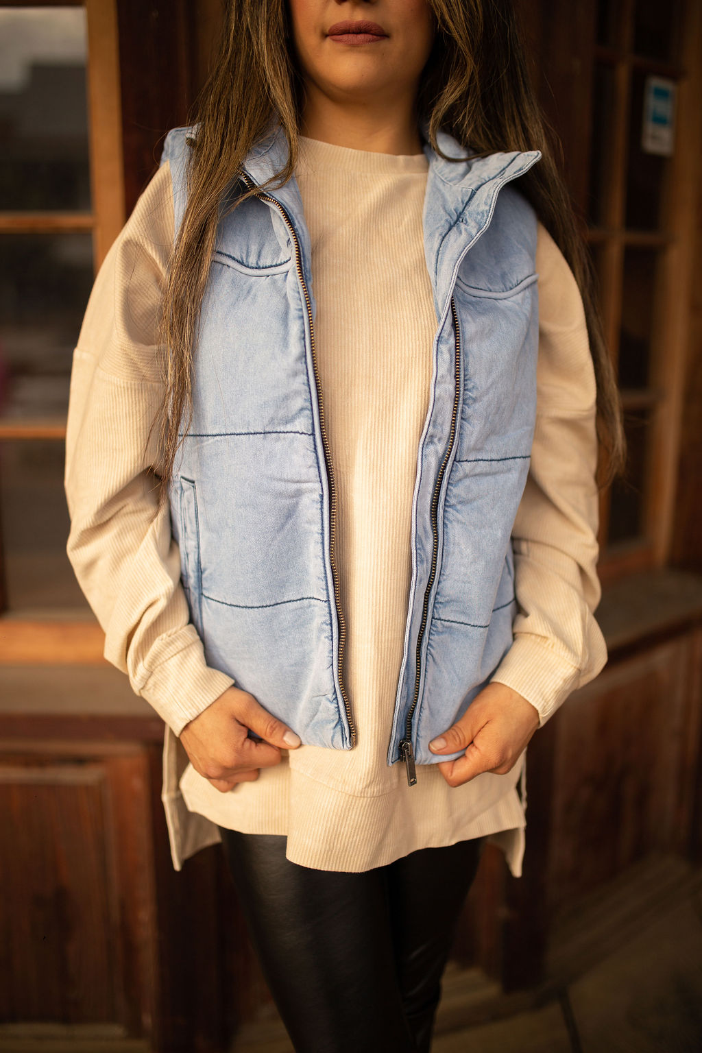 Light-wash denim puffer vest with quilted texture, high collar, and front pockets styled over a neutral long sleeve top.