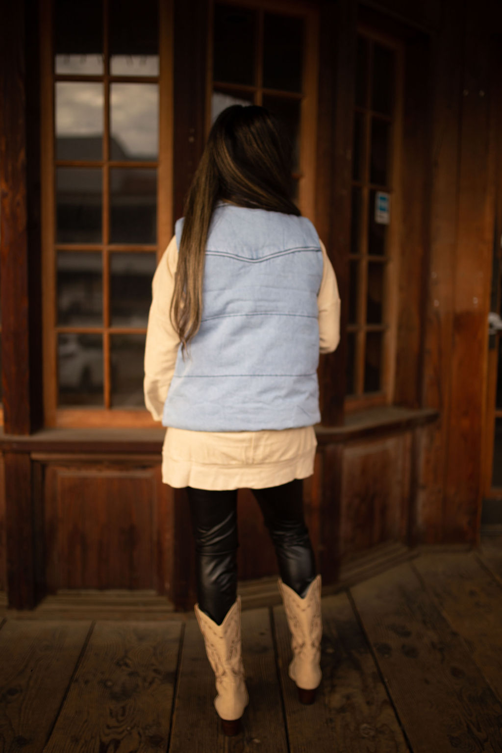 Light-wash denim puffer vest with quilted texture, high collar, and front pockets styled over a neutral long sleeve top.