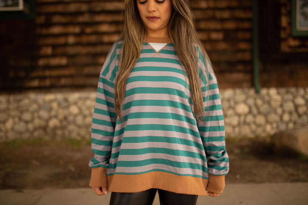 Teal and gray striped sweatshirt with caramel ribbed cuffs and hem, shown in natural outdoor lighting.